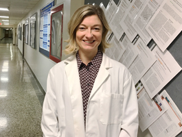 Woman with shoulder length blond hair wearing a lab coat smiles at the camera