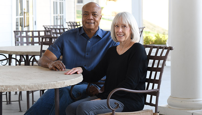 Two people sit at a table on an outdoor patio smiling toward the camera