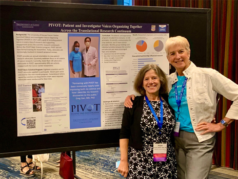 Two women stand in front of a scientific poster smiling
