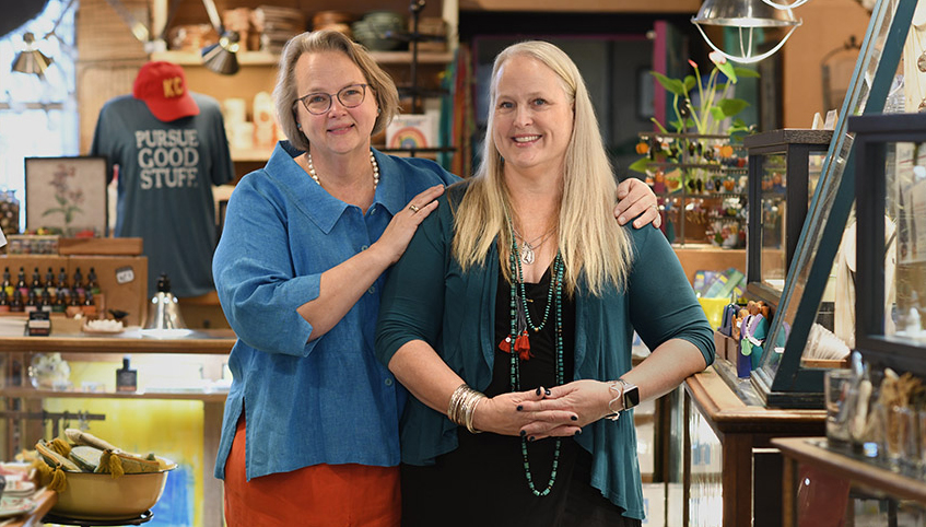 Two women in a retail store smile toward the camera