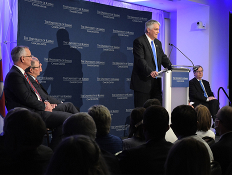 Dr. Jensen stands at a podium speaking while crowd watches