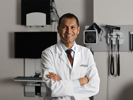 Dr. Bansal stands in front of medical equipment smiling toward the camera