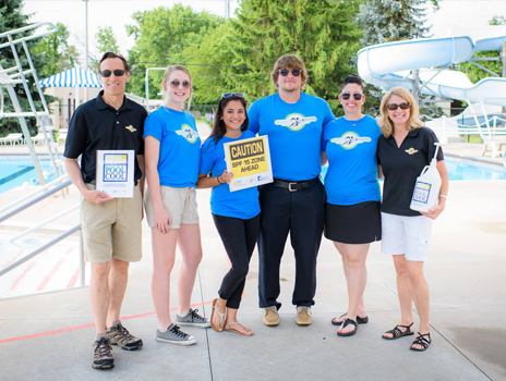 Group of people smile at the camera in front of an outdoor pool complex