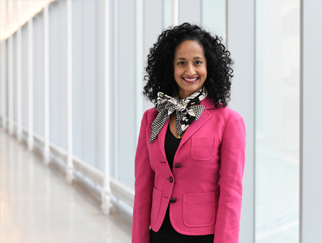 Woman with dark curly hair and bright pink blazer smiles at camera