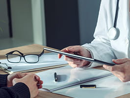 Close up of a desk top. It appears that two people are sitting at the desk as there is one pair of hands on one side of the desk and another pair holding a clipboard on the other side.