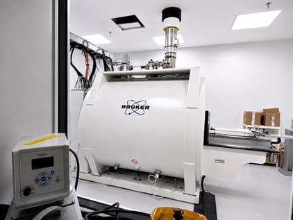 a large white cylindrical machine with a metallic tube and wire on top. The word "Bruker" is written on the side.