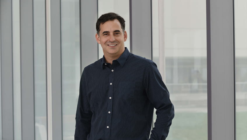 Dr. Bur stands in front of wall of windows smiling toward the camera