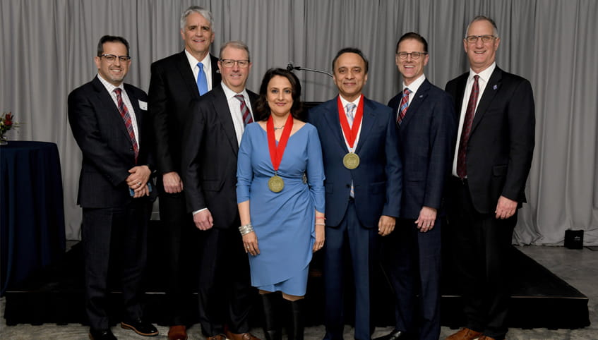Group of men in dark suits stand with woman in blue dress