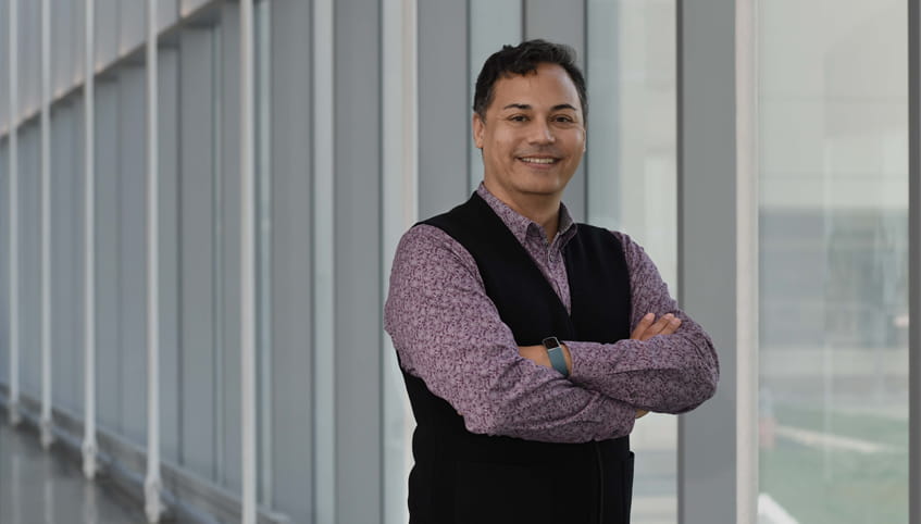 Dr. Lee stands in front of a wall of windows smiling at the camera