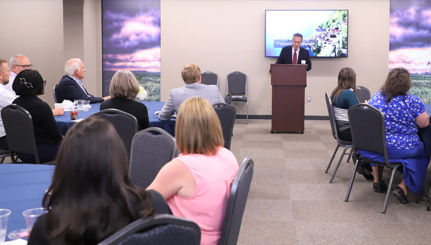 Man stands at podium while members of the audience look on