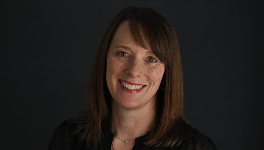 Woman with brown hair smiles with a grey background.
