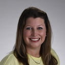 headshot of a person in a yellow blouse and shoulder length hair smiling at the camera