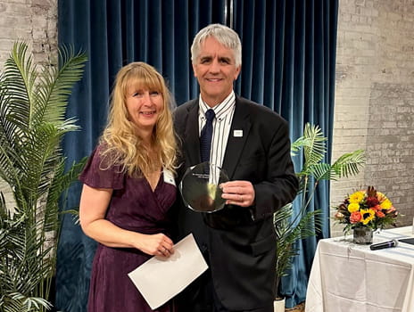 Susan Harp and Dr. Roy Jensen smile at the camera while holding an award
