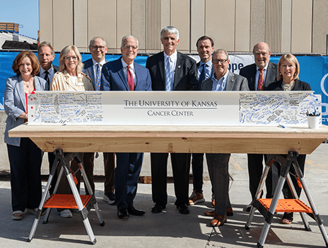 A group of people pose behind a steel beam covered in signatures.