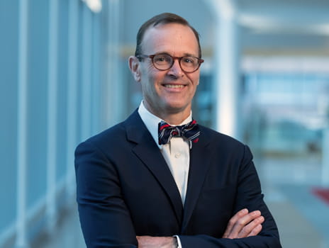 Man wearing glasses and a suit smiles at the camera
