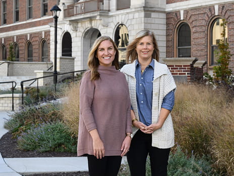 Two women stand outside next to each other smiling at the camera