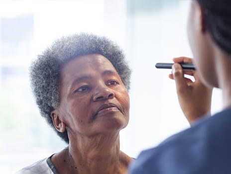 Middle aged black woman faces nurse who is checking her eyes with a small light