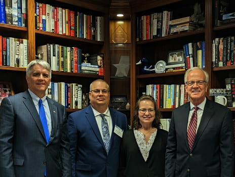 Four people stand together in front of a library wall