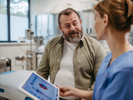 Female nurse in exam room showing information on a tablet to a middle aged male patient