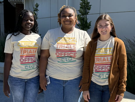 Three undergraduate students stand together outside the KU Cancer Center Clinical Trials Office.
