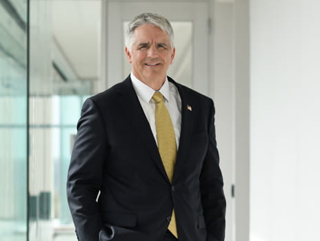 Man wearing a black suit with yellow tie smiles.