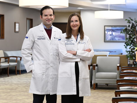 Two individuals stand in a clinic waiting room wearing white lab coats.