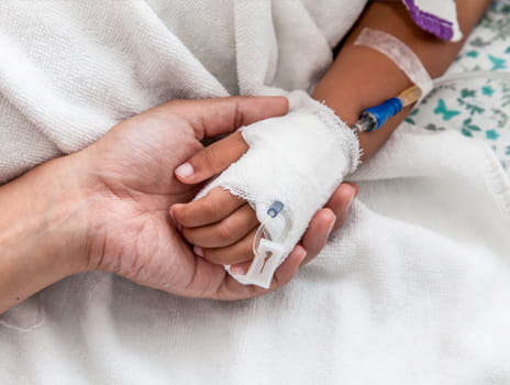 Close up image of a child's hand with IV tubes holding the hand of an adult.