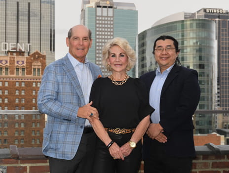 Three people stand together smiling at the camera with the Kansas City skyline in the background.