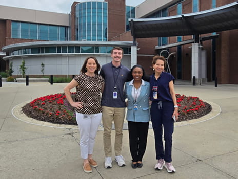 Group of four individuals stand together smiling outside of the Clinical Research Center.