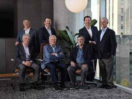 Seven men in business attire sit together inside of a office lobby.