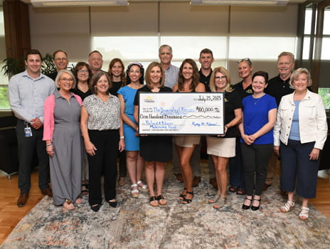 Group of people stand together holding large check