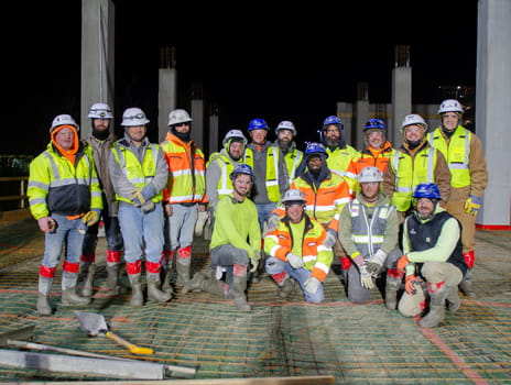 Photo of a group of people in construction gear standing together at a construction site at dawn