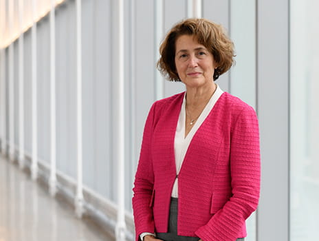 Woman in pink blazer and short curly brown hair stands in front of a panel of windows