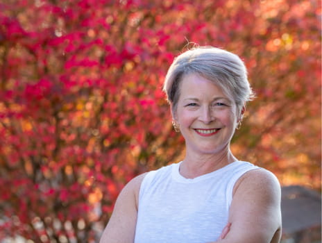 Dawn Wheeler smiling outside in front of a tree with beautiful red and orange leaves