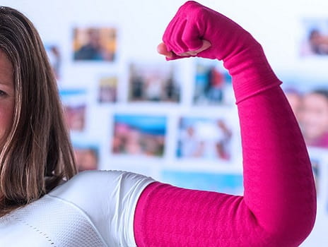 A pink lymphedema compression sleeve and glove on a woman's flexed bicep.