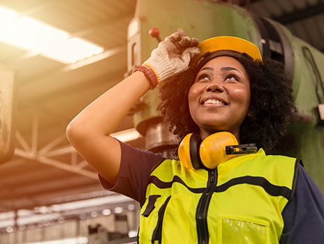 woman tilting hard hat, looking up, standing in front of machinery in a factory